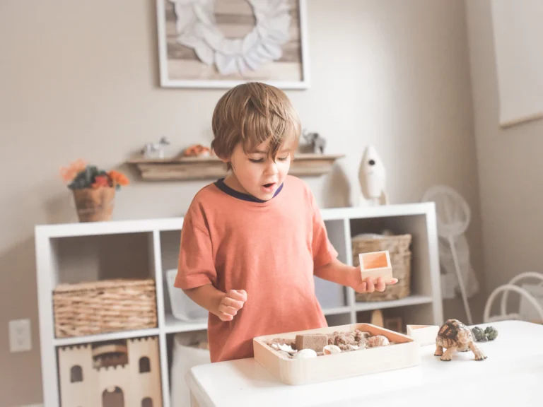 Boy in orange crew neck t-shirt standing in front of white wooden table with cupcakes