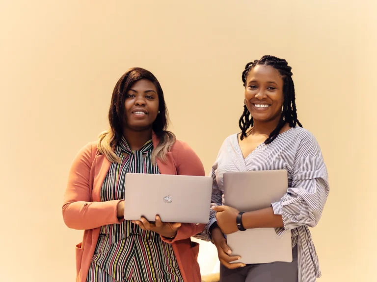 Two women standing next to each other holding laptops