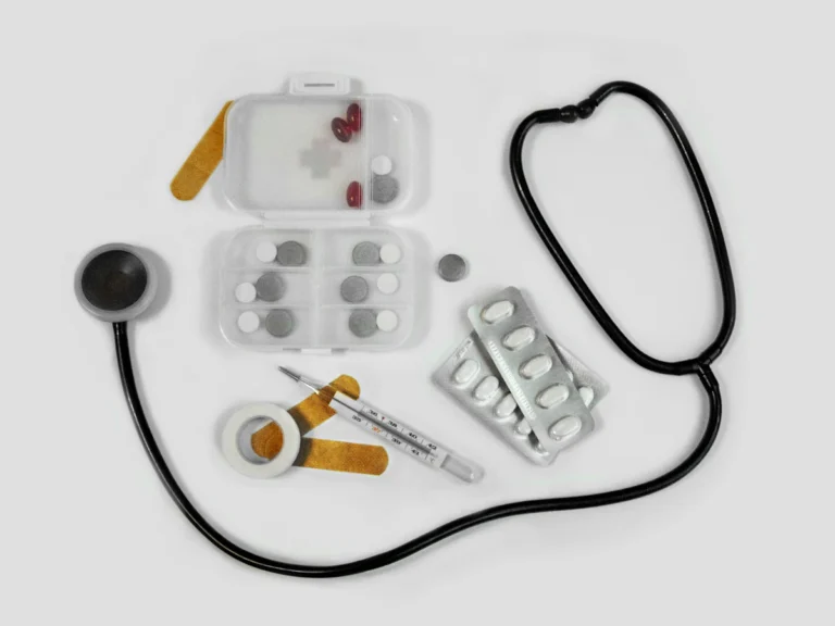 A stethoscope, pill organizer, blister packs, thermometer, and adhesive bandages on white