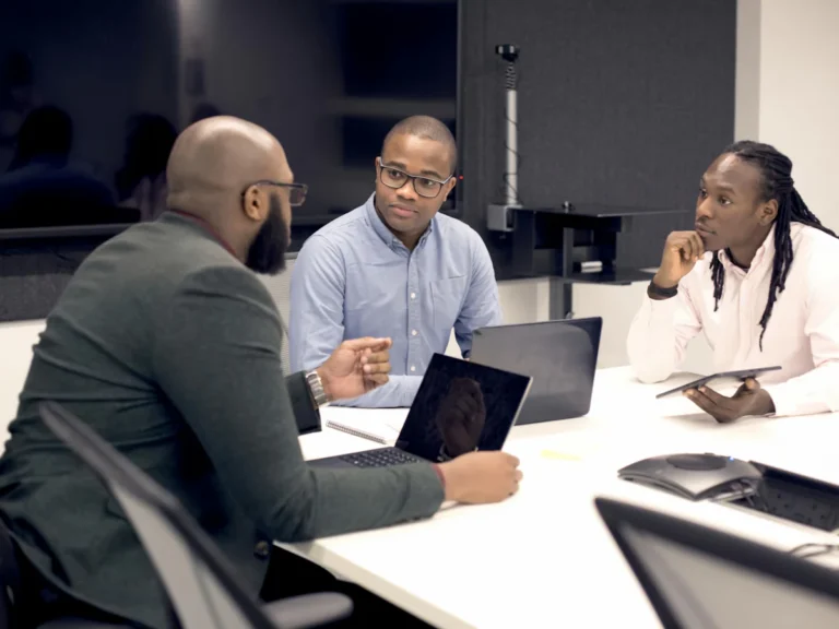 A group of people sitting around a table with laptops