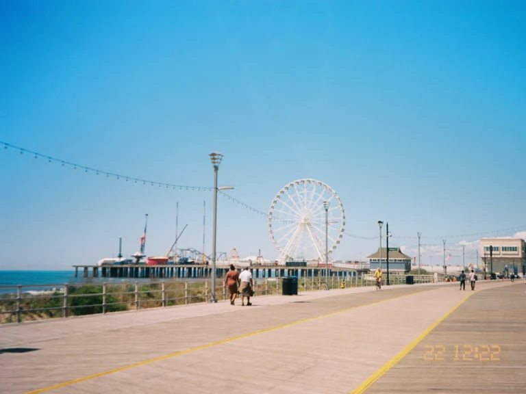 A boardwalk with a ferris wheel on a pier under a clear blue sky