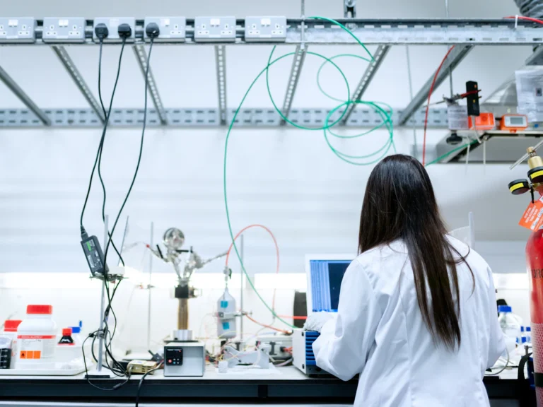A scientist in a white lab coat using a laptop in a laboratory