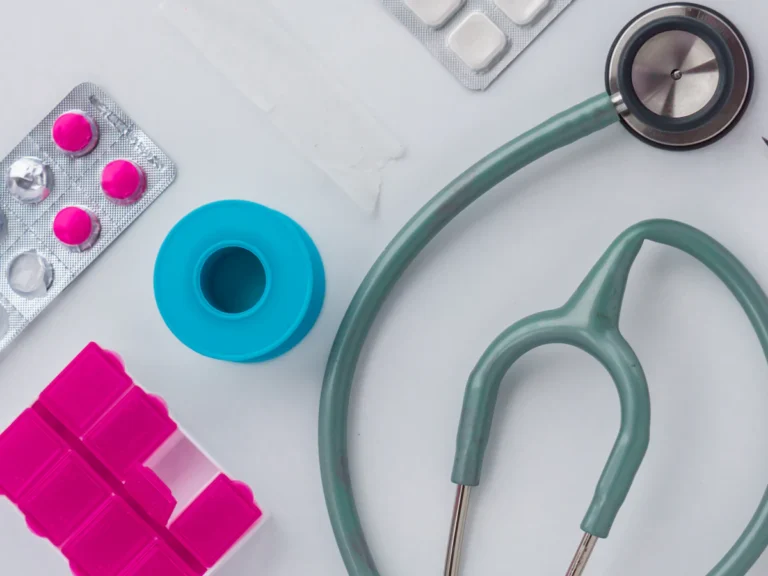 A stethoscope, pink pills, blue tape, and scissors on a white surface
