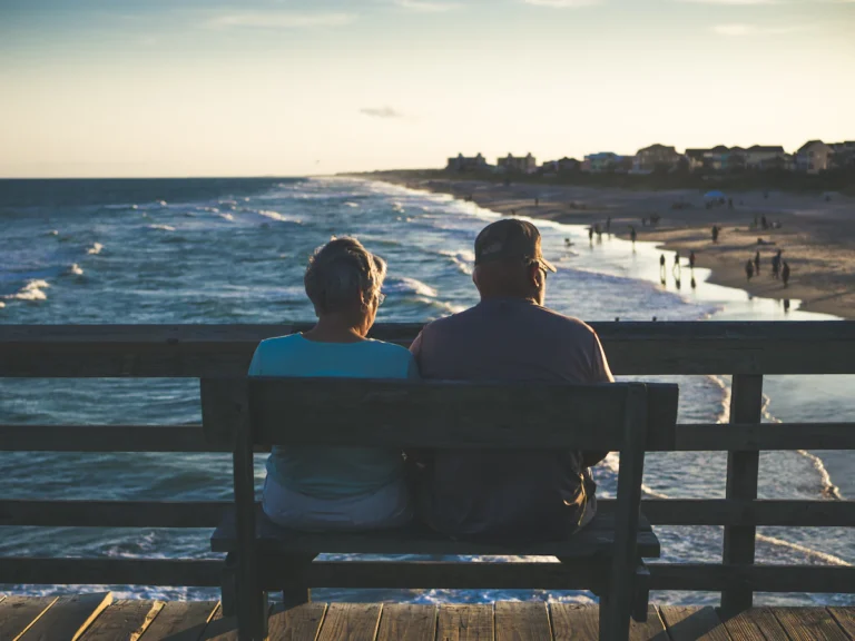 Man and woman sitting on bench in front of beach