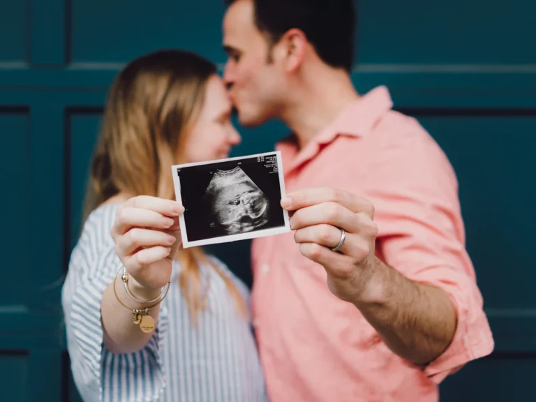 Man kissing woman's forehead white holding ultrasound photo