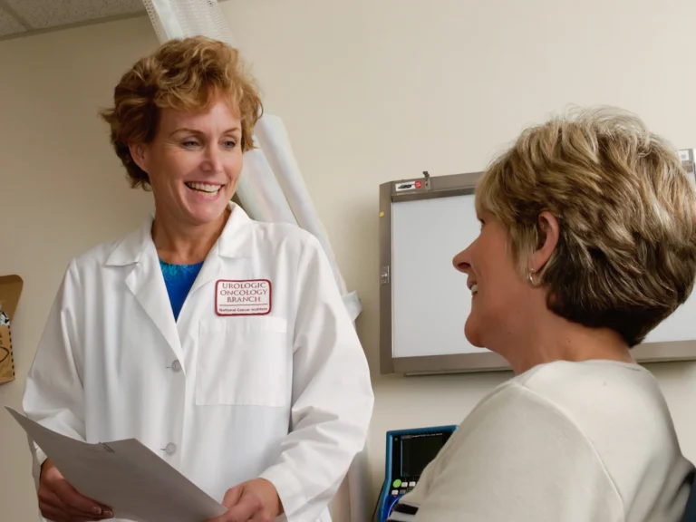 A smiling doctor in a white coat talking to a patient in a clinic