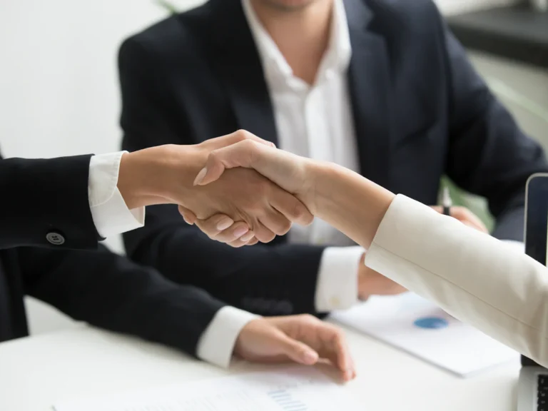 Two people shaking hands in front of a laptop
