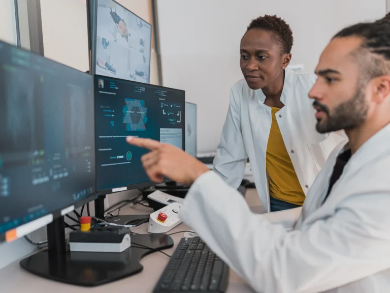 Two medical professionals in white coats reviewing digital imaging on computer monitors