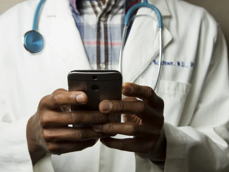 Person wearing lavatory gown with green stethoscope on neck using phone while standing