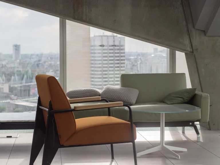 Orange fabric padded armchair with black metal base near round clear glass-top table and gray sofa